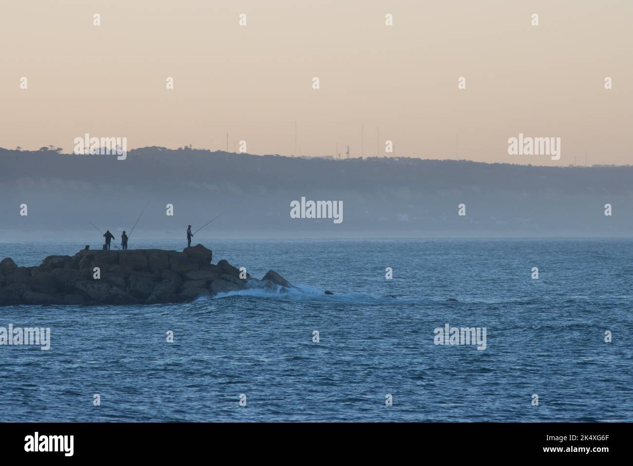 Fishers on the oceans - groupe of men stand on the coast of the sea with fishing rod at sunrise Stock Photo