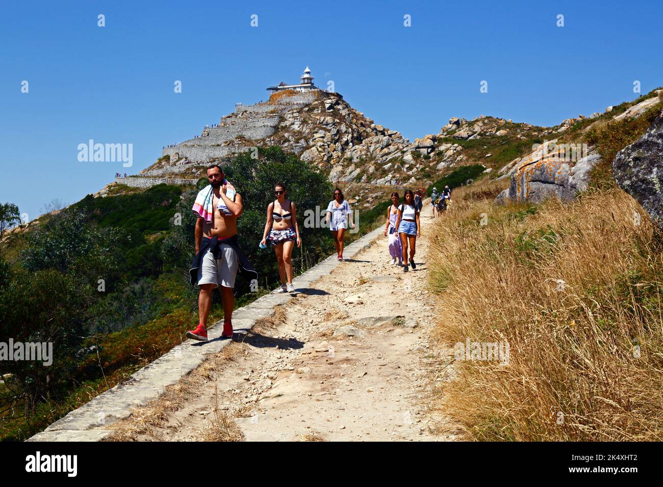 Tourists hiking on the trail up to the summit (with a lighthouse) of Illa de Faro or Montefaro, Cies Islands,Galicia, Spain Stock Photo