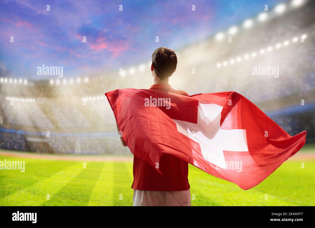 Switzerland football supporter on stadium. Swiss fan on soccer pitch watching team play. Young player with flag and national jersey Stock Photo