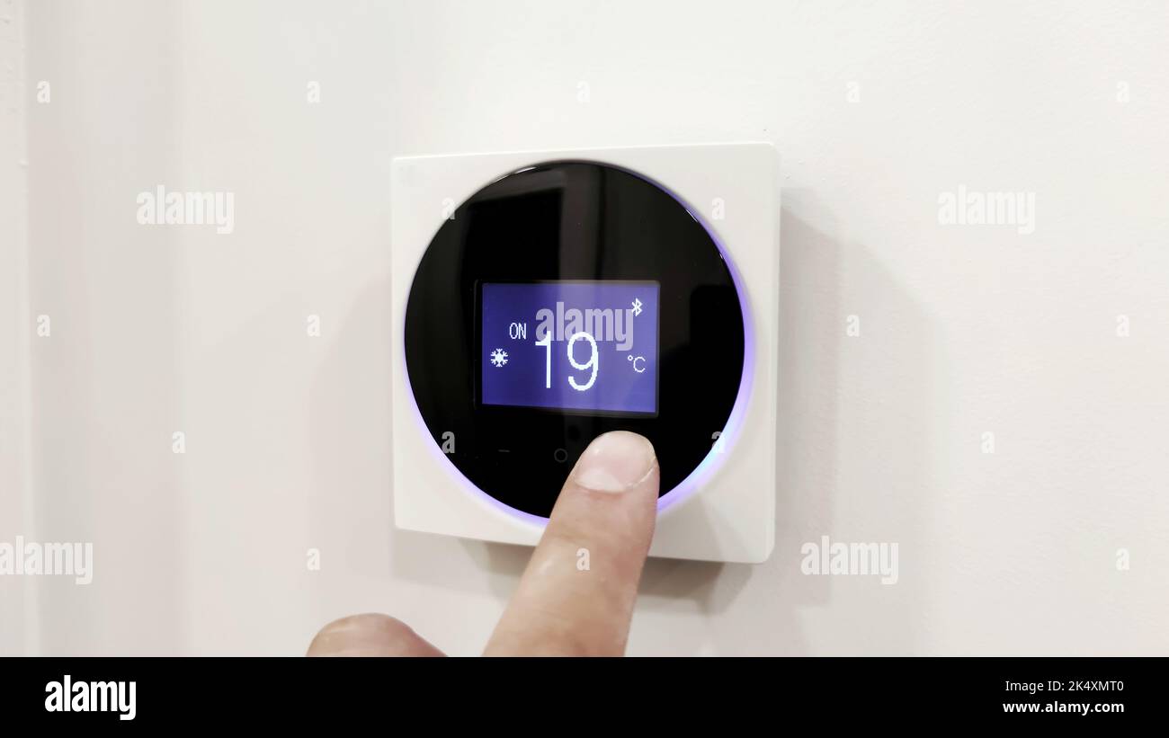Wall-mounted digital climate control, home thermostat that controls a smart modern and contemporary home concept. fingers set a comfortable Stock Photo