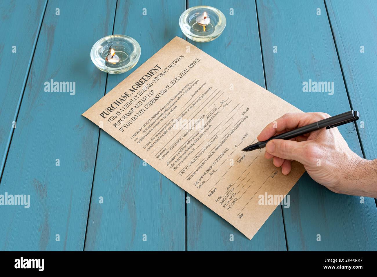 Man with fountain pen signing contract next to lit candles. Stock Photo