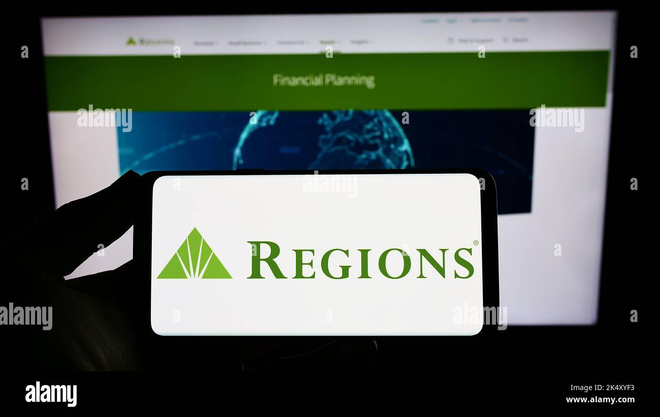 Person holding smartphone with logo of US banking company Regions Financial Corporation on screen in front of website. Focus on phone display. Stock Photo