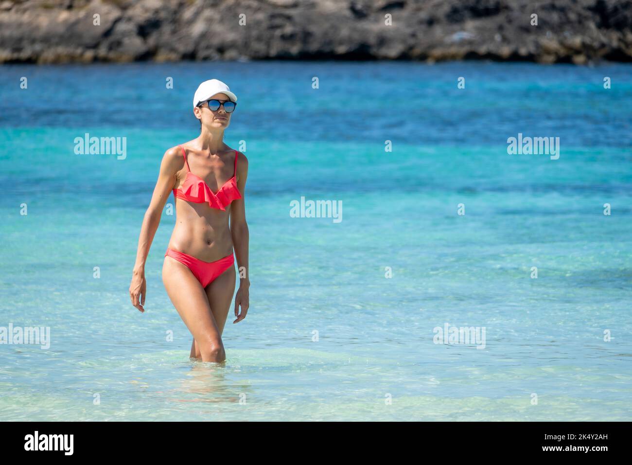 Brunette woman with coral bikini and cap posing on the beach Stock Photo