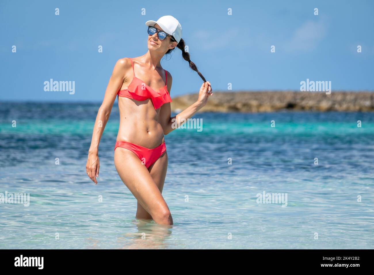 Brunette woman with coral bikini and cap posing on the beach Stock Photo