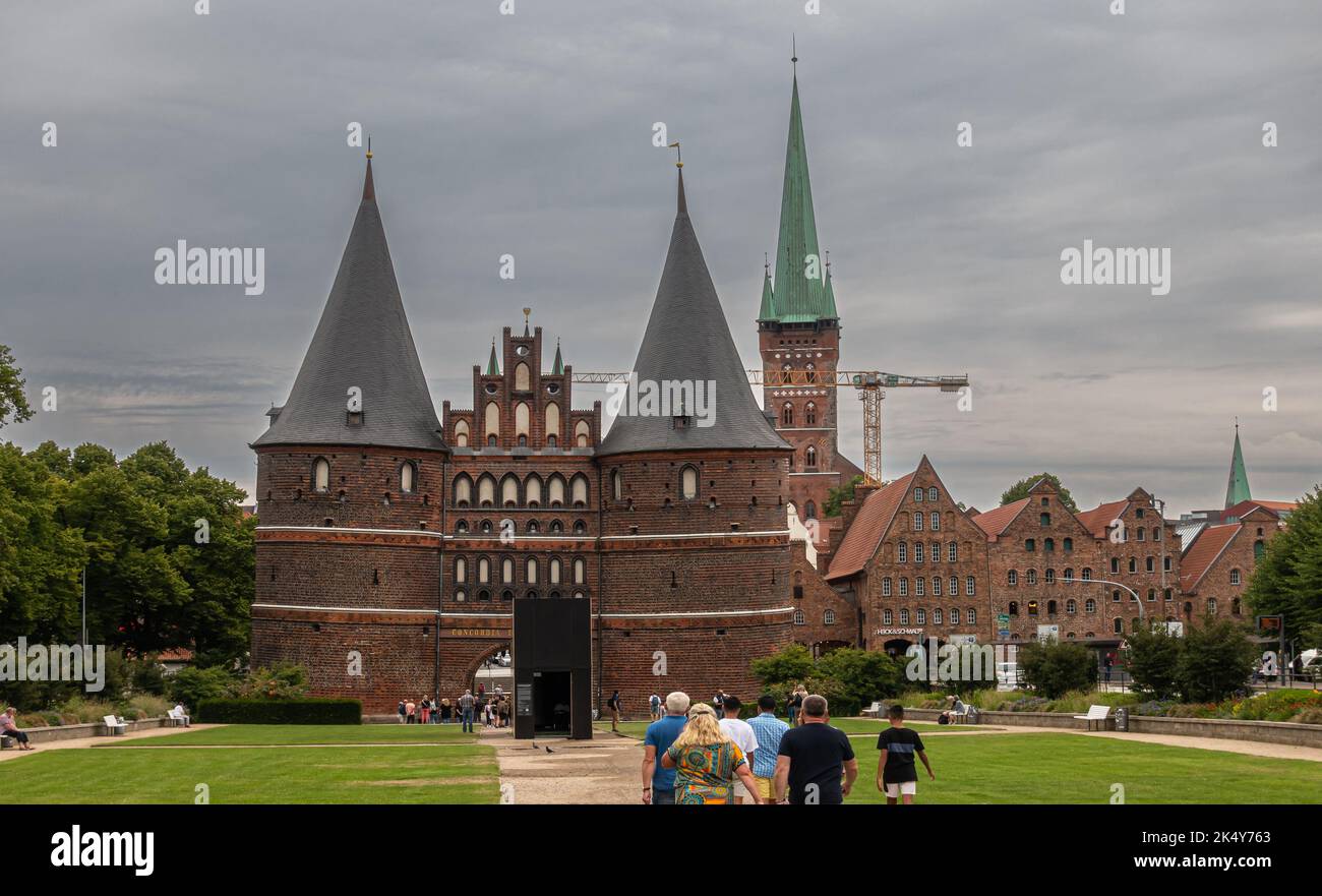 Germany, Lubeck - July 13, 2022: Historic Holsten Gate, Tor, with St. Petri, Peter, church in back under heavy gray sky. Green park in front. Construc Stock Photo