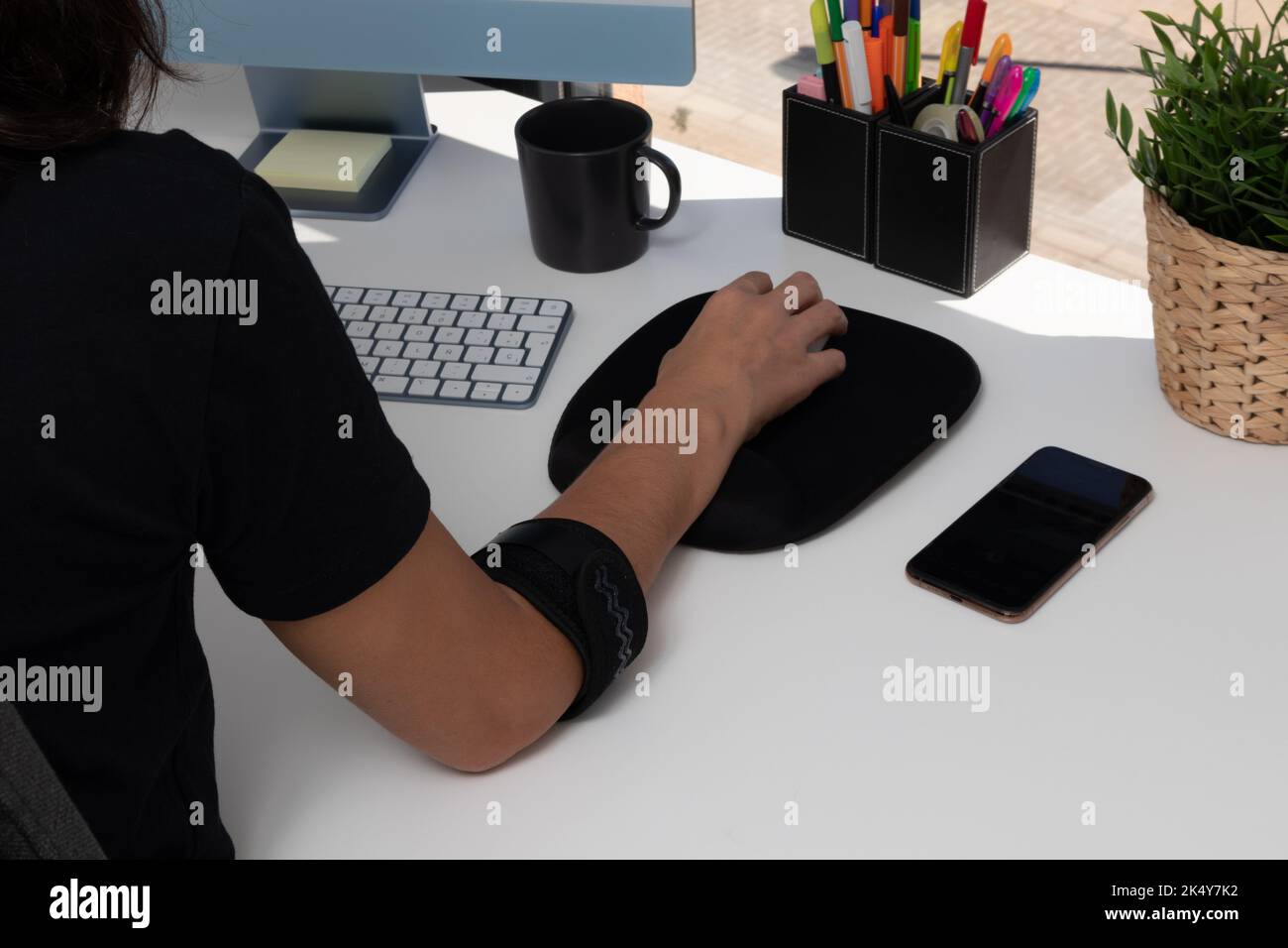 unrecognizable woman working at computer with tendonitis caused by mouse use, wearing an elbow