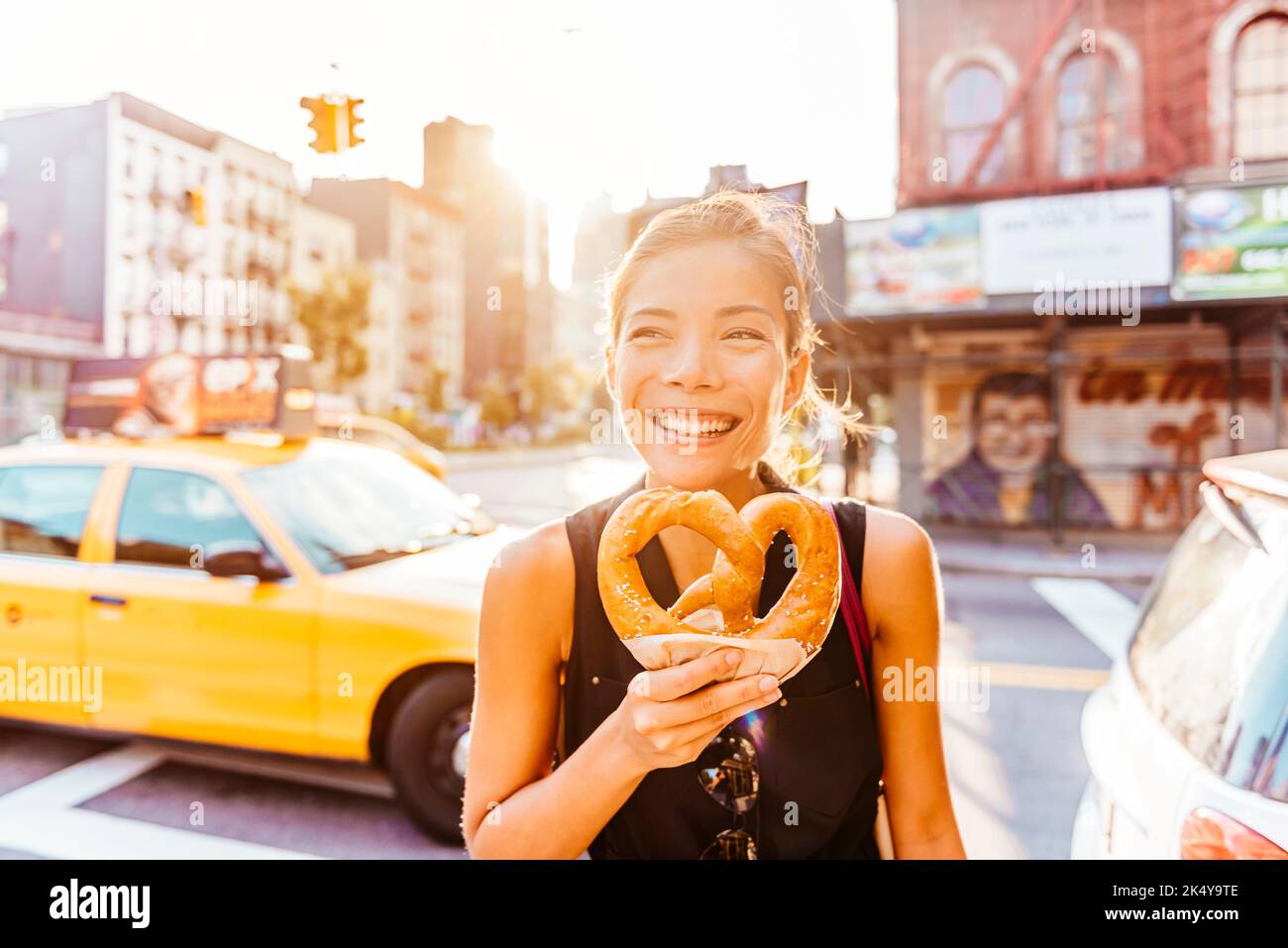 New York people lifestyle photo. Woman eating pretzel in Manhattan, a classic New York City snack. Multiracial asian young professional portrait Stock Photo