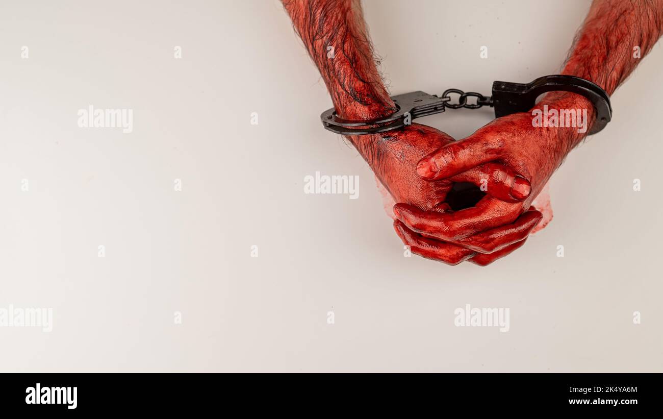 Bloodied male hands in handcuffs, folded on a white table. Stock Photo