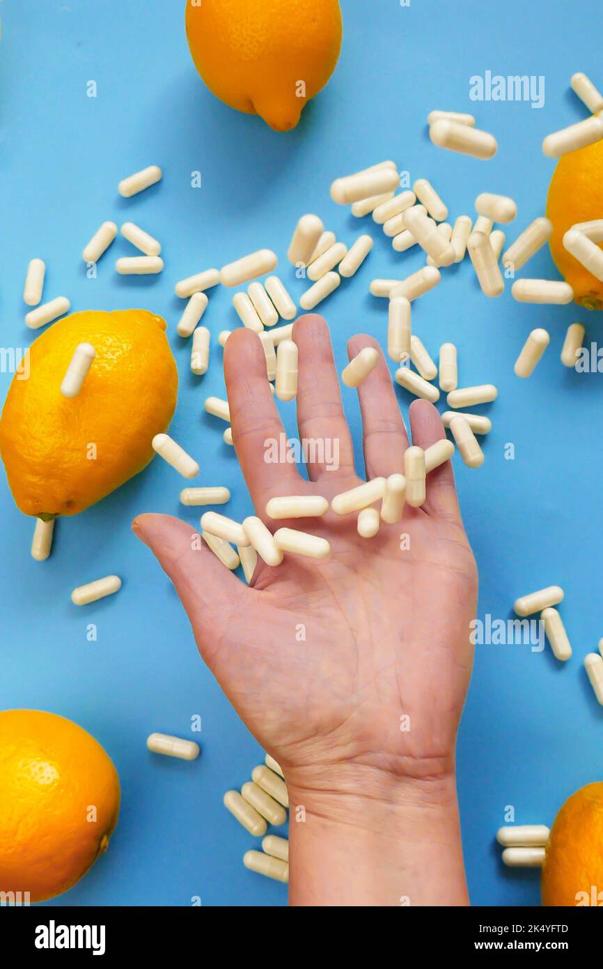 White capsules of vitamin C in a hand and yellow lemon citrus fruits