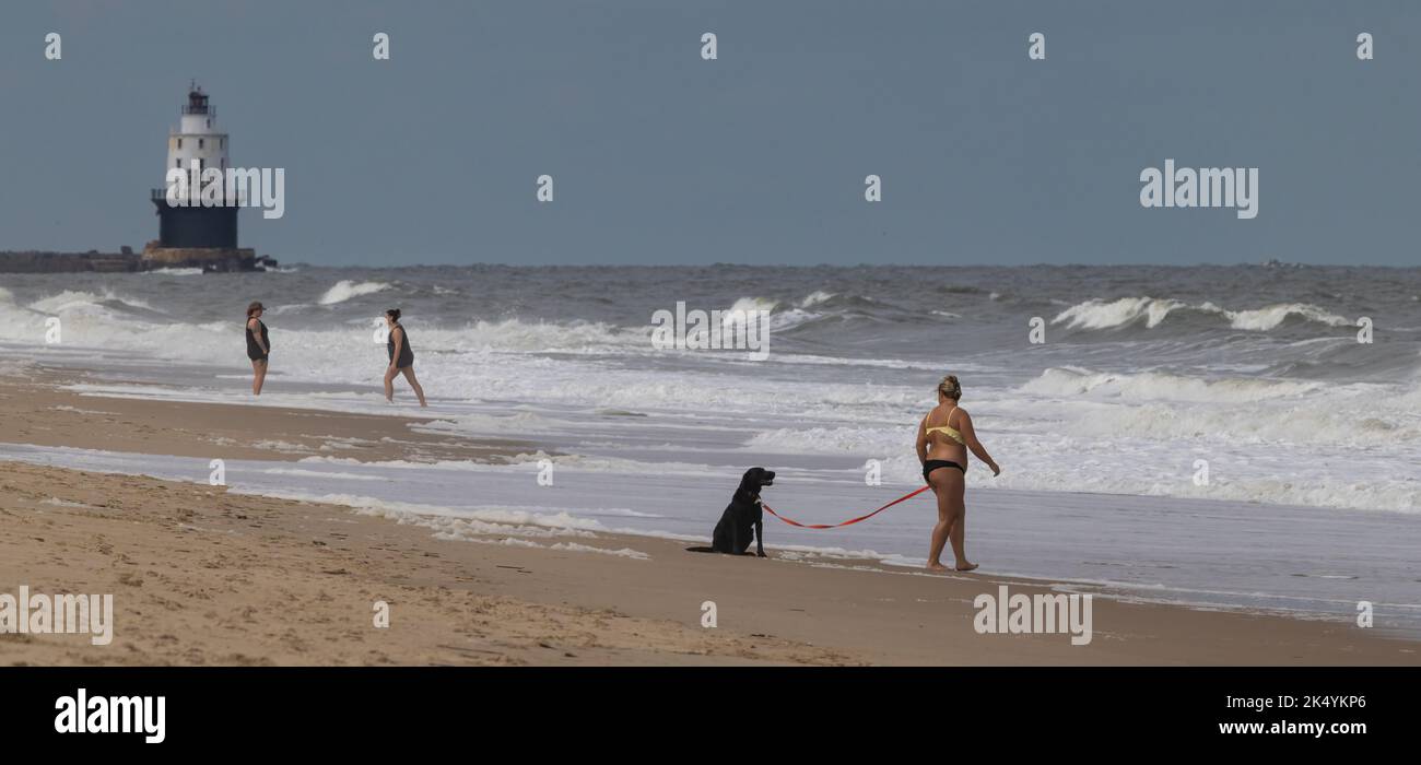 3 people and a dog at the beach with the Harbor of Refuge Lighthouse in