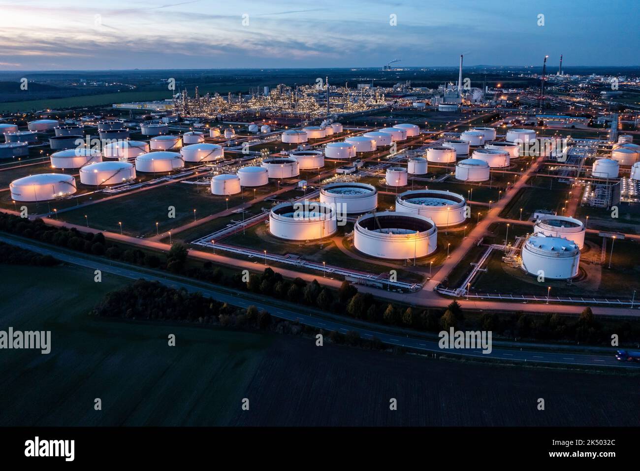 04 October 2022, Saxony-Anhalt, Leuna: Behind the illuminated tank farm, the facilities of the Total refinery and the chemical park rise into the air (aerial view with drone). The refinery, built in 1997 by the French mineral oil company Elf-Aquitaine, is celebrating its 25th anniversary on the same day. Around 12,000 people work in various companies at the 1300-hectare chemical site in Leuna, including around 600 in the refinery. Every year, gasoline, diesel, heating oil, liquefied petroleum gas, aviation fuels, bitumen, methanol and other specialty chemical products are produced here from up Stock Photo