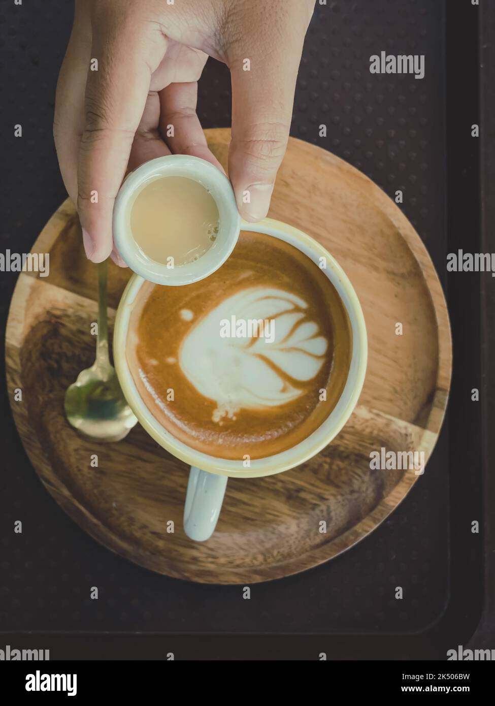 Hand of young woman pouring condensed milk into hot cappuccino on cafe ...