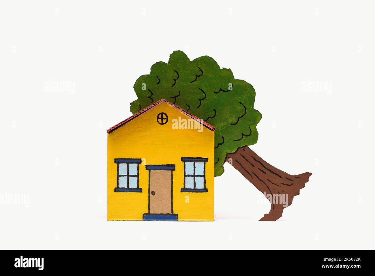 A yellow and red toy cardboard house with a tree in its roof in the middle of frame isolated on a white background, captured in a studio Stock Photo
