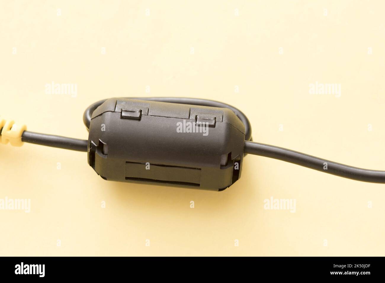 Close up of a black ferrite bead attached to a cable, isolated on a plain background. Stock Photo