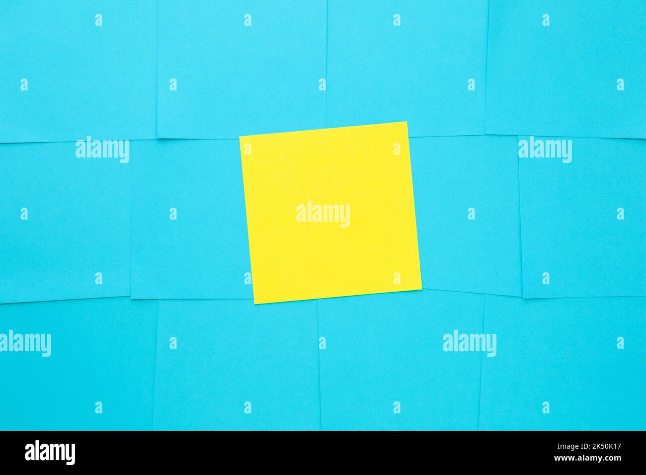 Multiple blank blue sticky notes and one yellow in the middle on bulletin board. Stock Photo