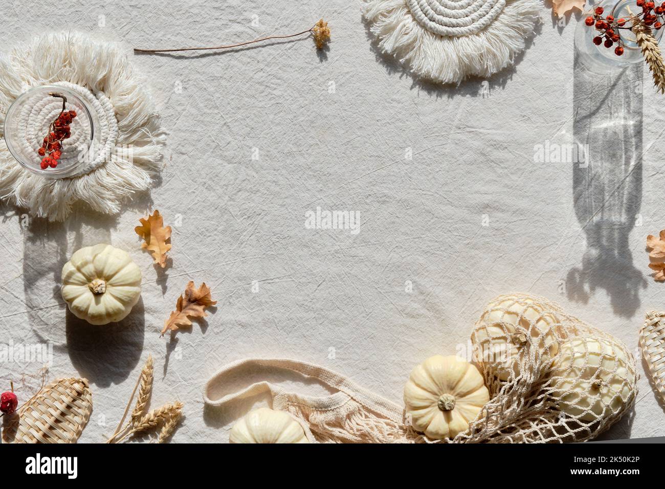 Off white textile background with natural Fall decorations. Flat lay, top view. Pumpkins in net bag, dry leaves, macrame pads, wattle leaves and straw Stock Photo