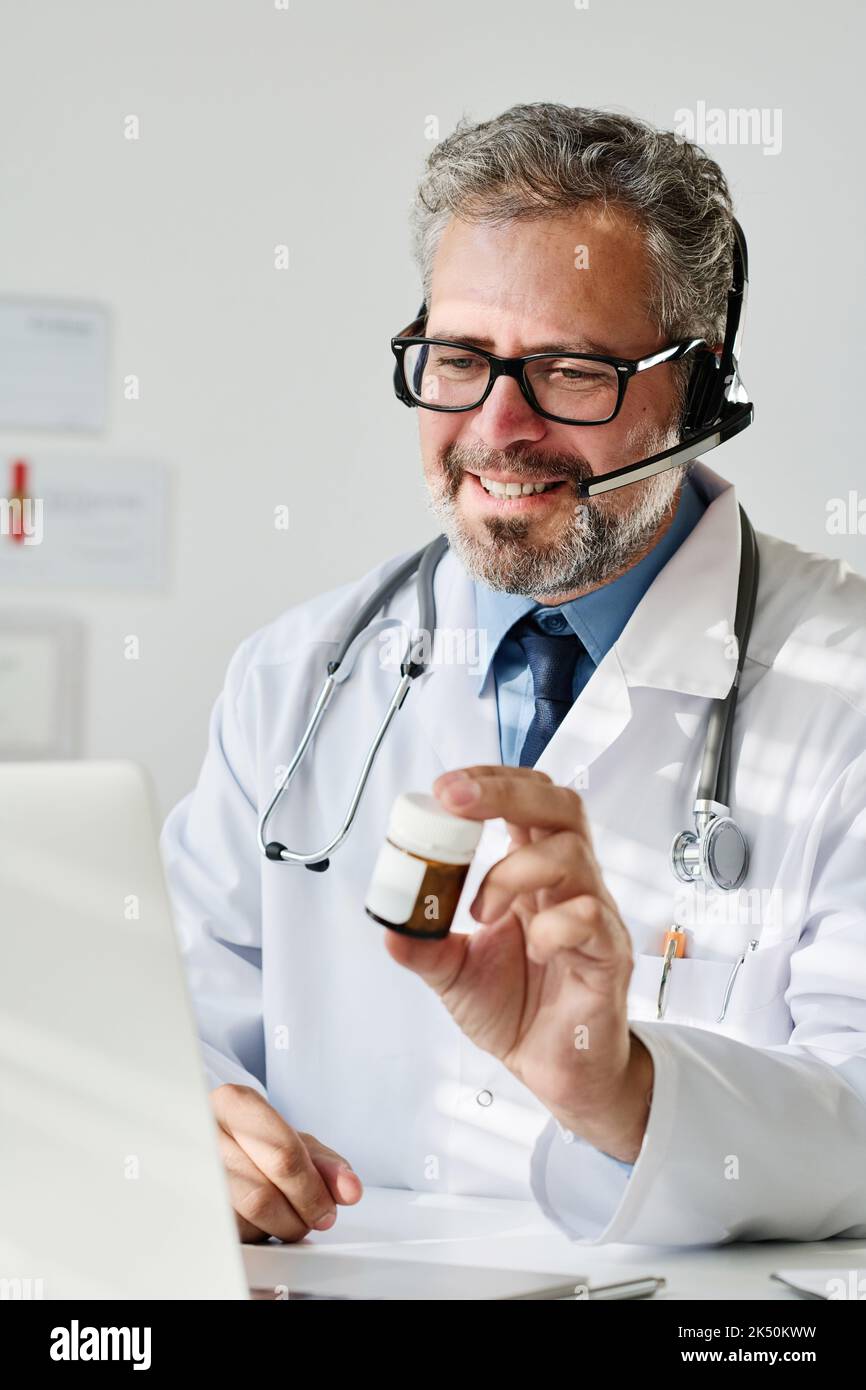 Mature doctor in eyeglasses and headphones prescribing medicine to