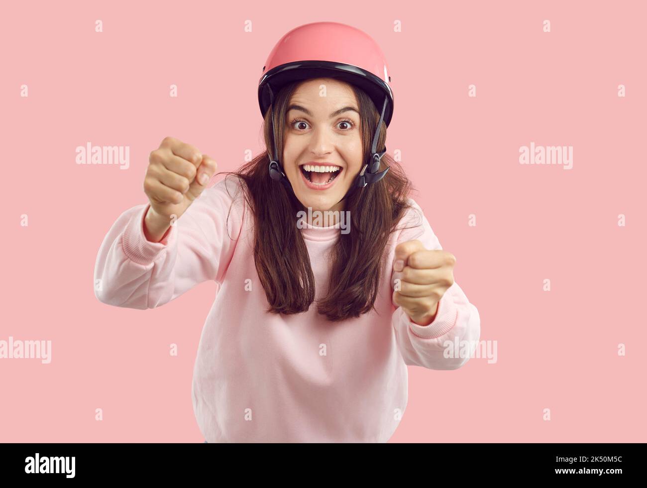 Funny happy excited young woman in pink helmet pretending to drive invisible car Stock Photo
