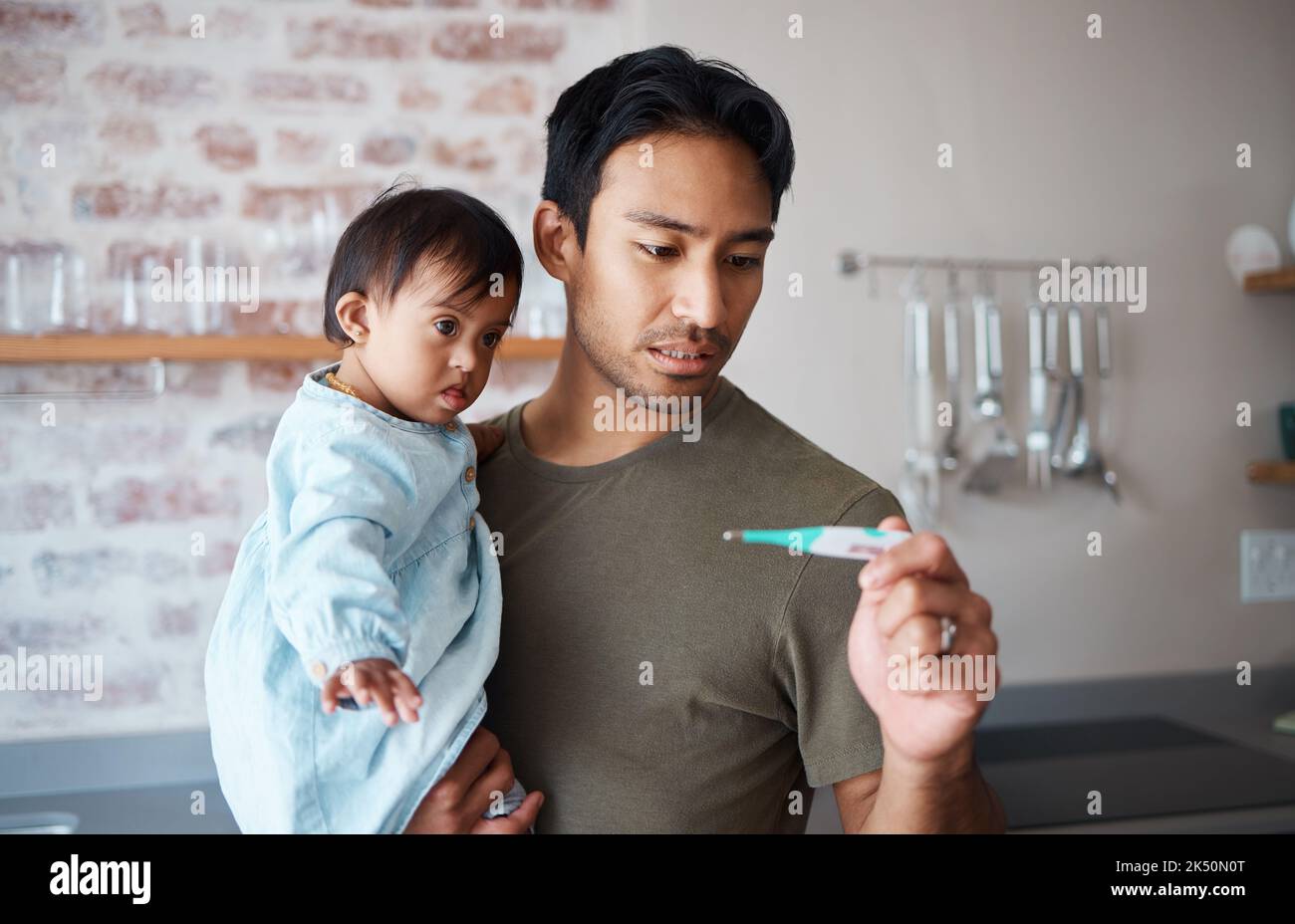 Down syndrome, thermometer and parent worried about baby health, checking fever and temperature in a kitchen. Love, disability and child care with Stock Photo