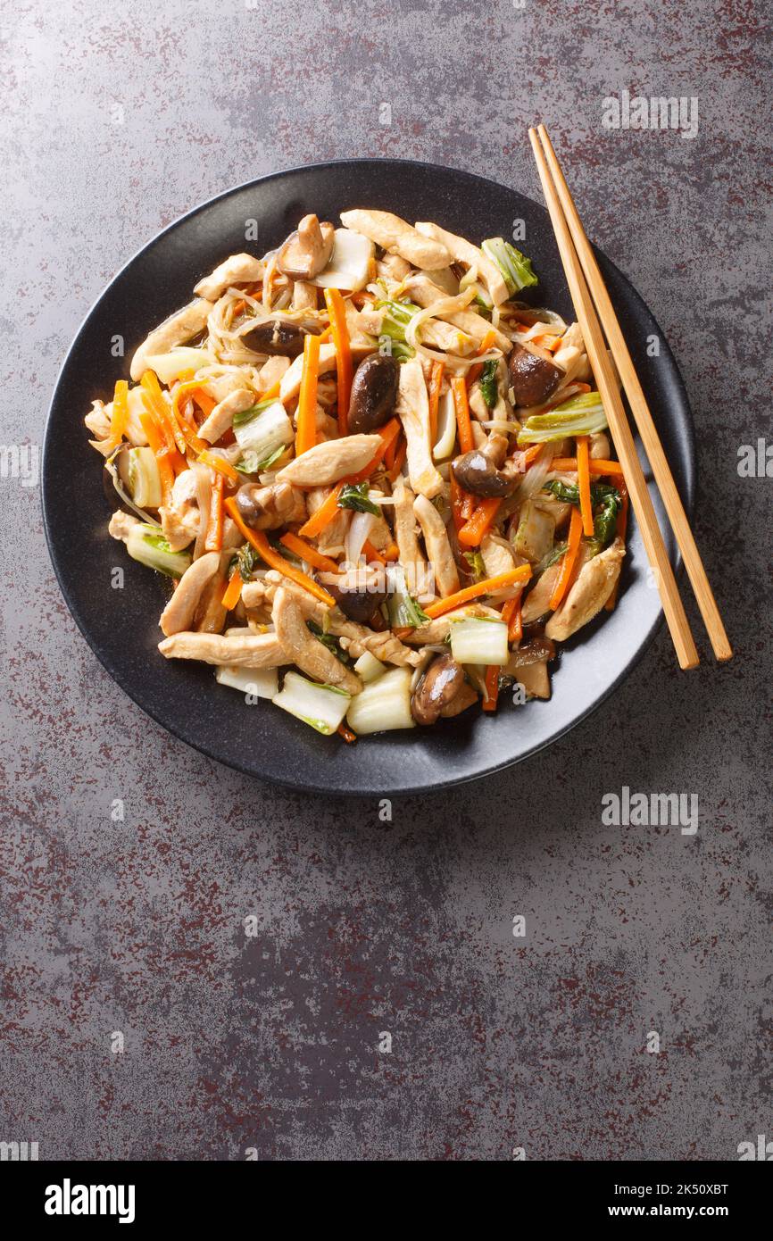 Chop Suey fried chicken with mushrooms, bok choy, onion, bean sprouts and carrots close-up in a plate on the table. Vertical top view from above Stock Photo