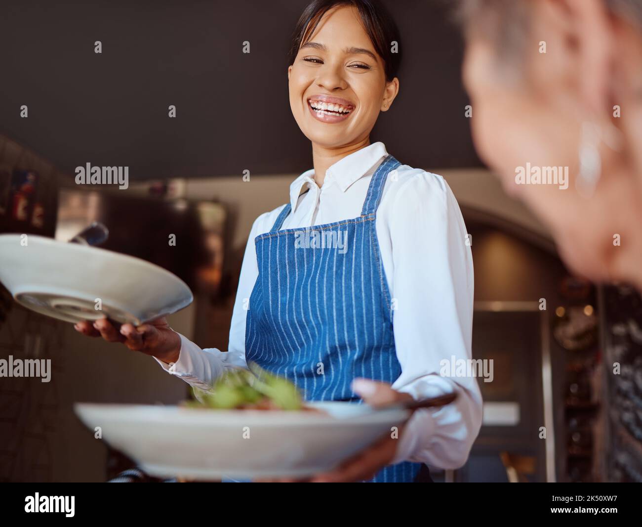 Waitress in a restaurant, serving customer her food, healthy salad and gives service with a smile. Woman in the hospitality industry, friendly laugh Stock Photo
