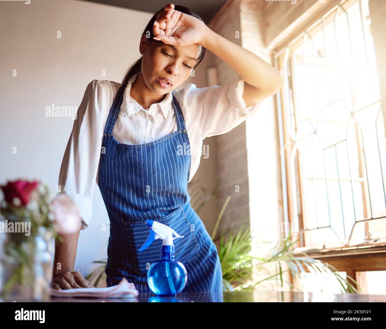 Cleaning house, burnout and tired cleaner working hard on dirty table and furniture feeling exhausted. Unhappy, frustrated and sweaty woman overworked Stock Photo