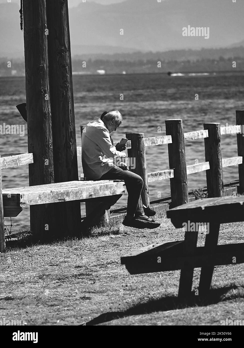 A vertical grayscale shot of old friends sitting on a bench seaside on the seaside in Whidbey Island Stock Photo