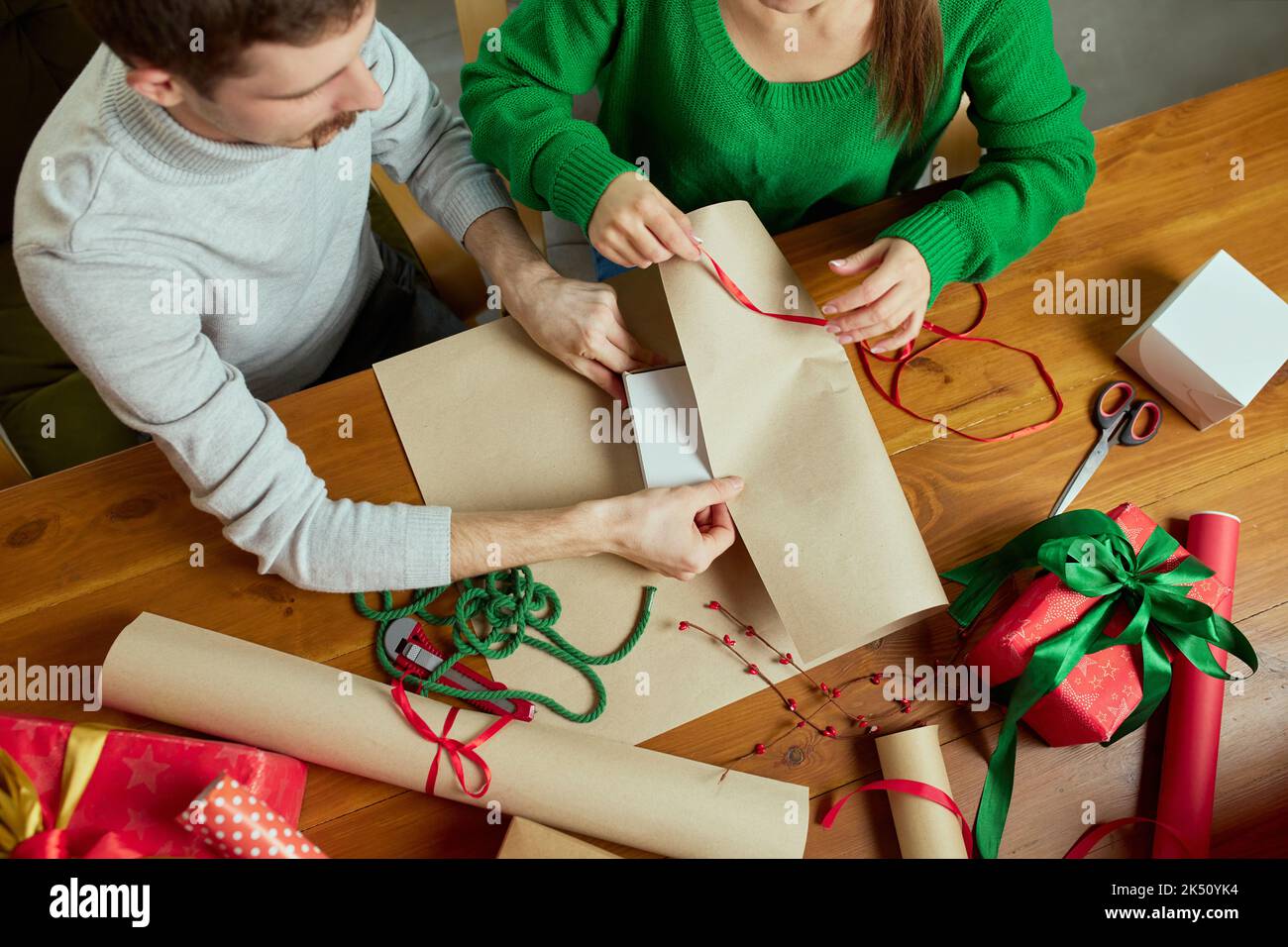 Top view image of man and woman wrapping gifts together, using wrapping