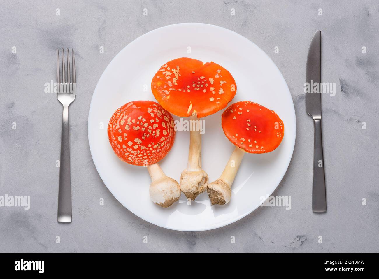 Amanita muscaria fly agaric poisonous mushrooms on plate with fork and knife top view. Consumption of hallucinogenic mushroom concept Stock Photo