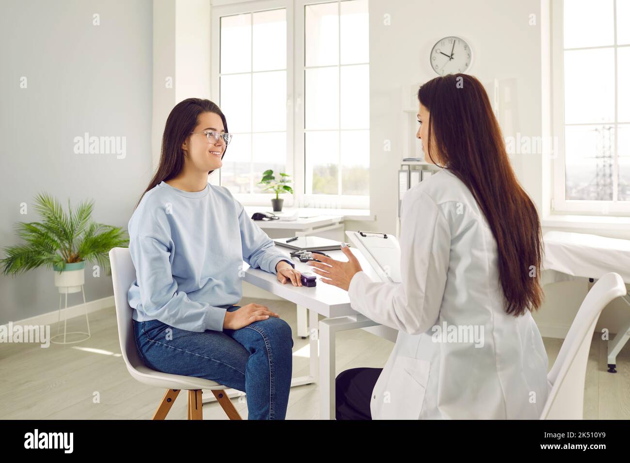 Satisfied female patient uses pulse oximeter while talking to doctor at hospital appointment. Stock Photo