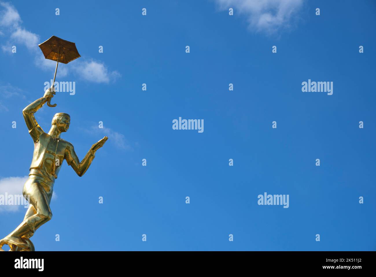 A fun gold sculpture of a boy riding a unicycle, holding an umbrella ...