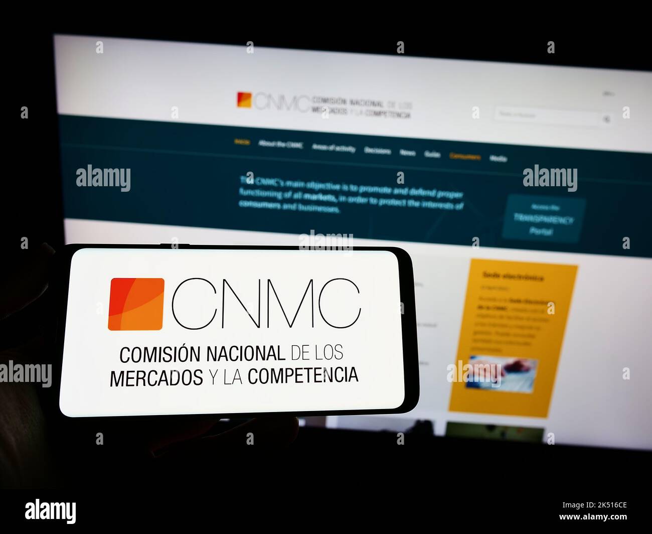 Person holding smartphone with logo of Spanish competition regulator CNMC on screen in front of website. Focus on phone display. Stock Photo