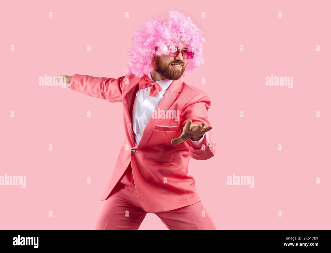 Funny bearded man in wig, glasses and suit having fun isolated on pink background. Stock Photo