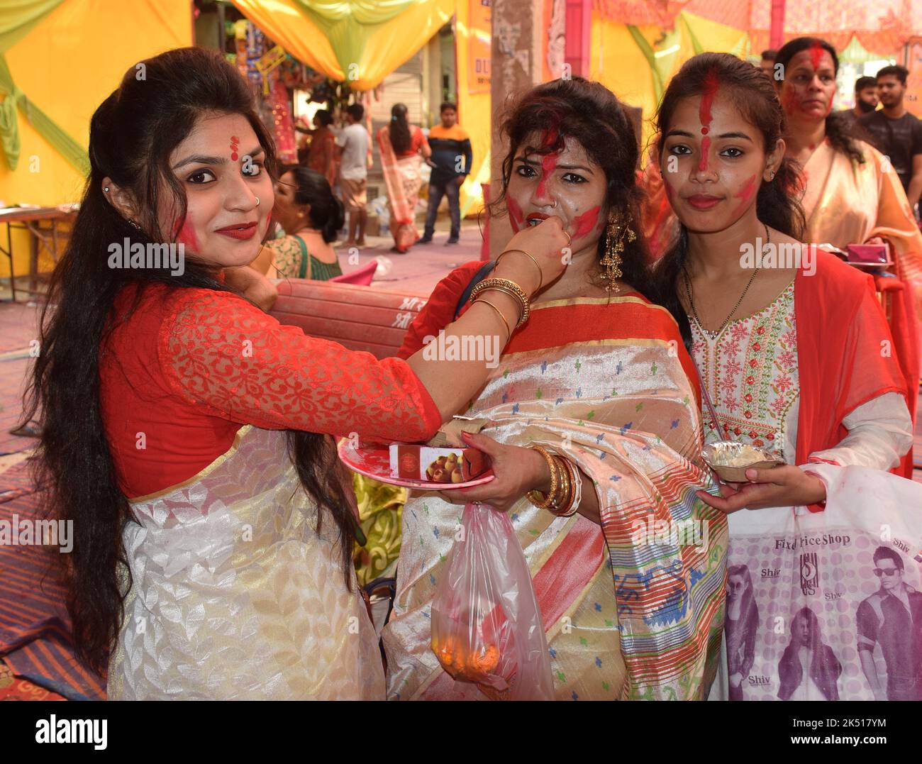 Happy Bengali Ladies in tradition attire offering sweets to each other during Vijaya Dashami celebration in India Stock Photo