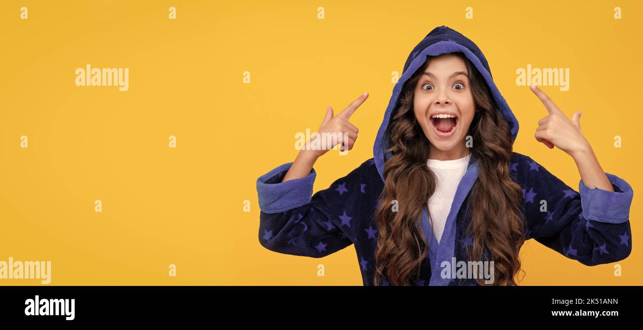 Excited child in hooded bathrobe happy screaming pointing fingers yellow background, point. Child face, horizontal poster, teenager girl isolated Stock Photo