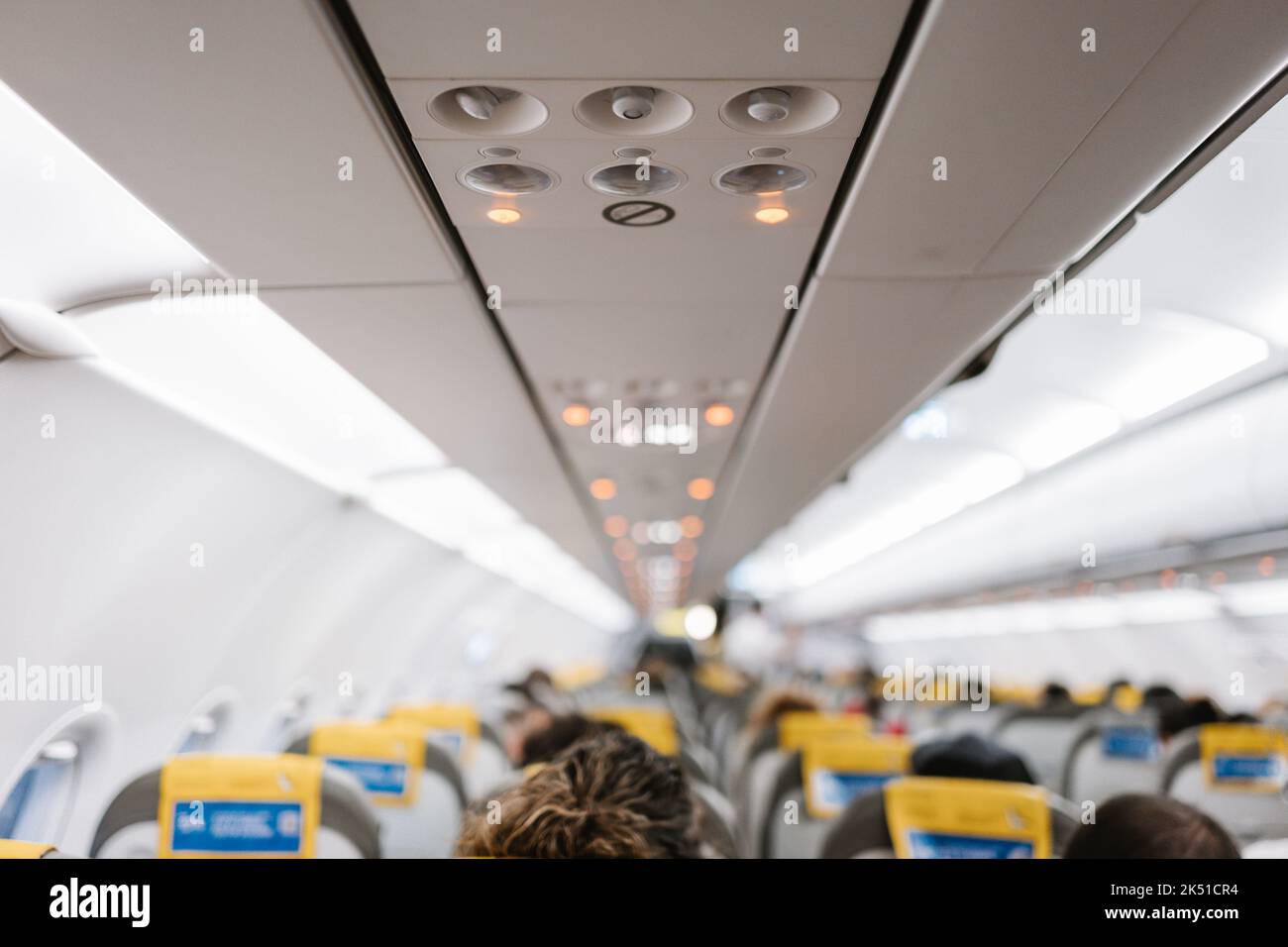 Unrecognizable passengers sitting on comfortable chairs under control panel inside contemporary aircraft during trip Stock Photo