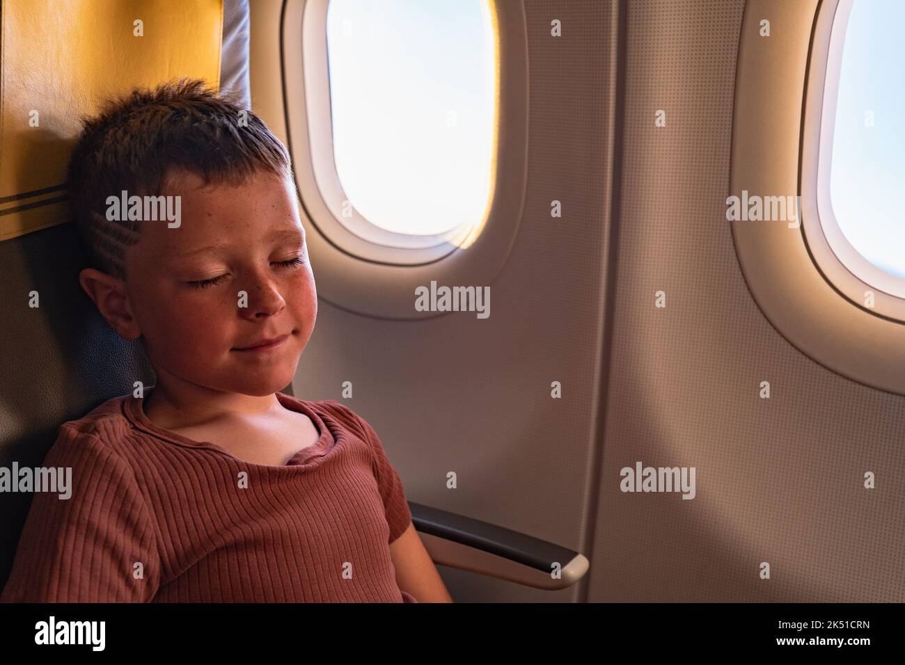 High angle of calm boy smiling while sitting on chair and sleeping near windows in plane Stock