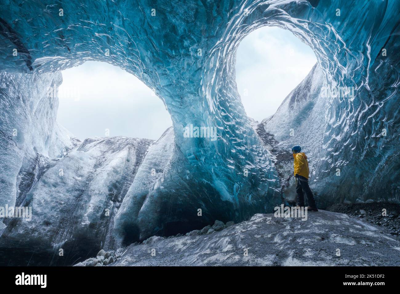 Tourist in outerwear standing near uneven holes in ice surface while exploring cave in Vatnajokull Glacier on winter day in Iceland Stock Photo
