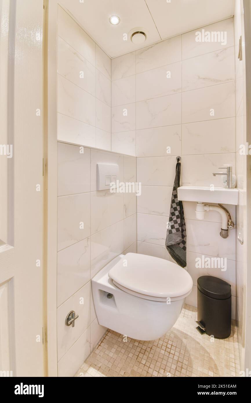 Wall hung toilet and small sink in corner in lavatory room with beige