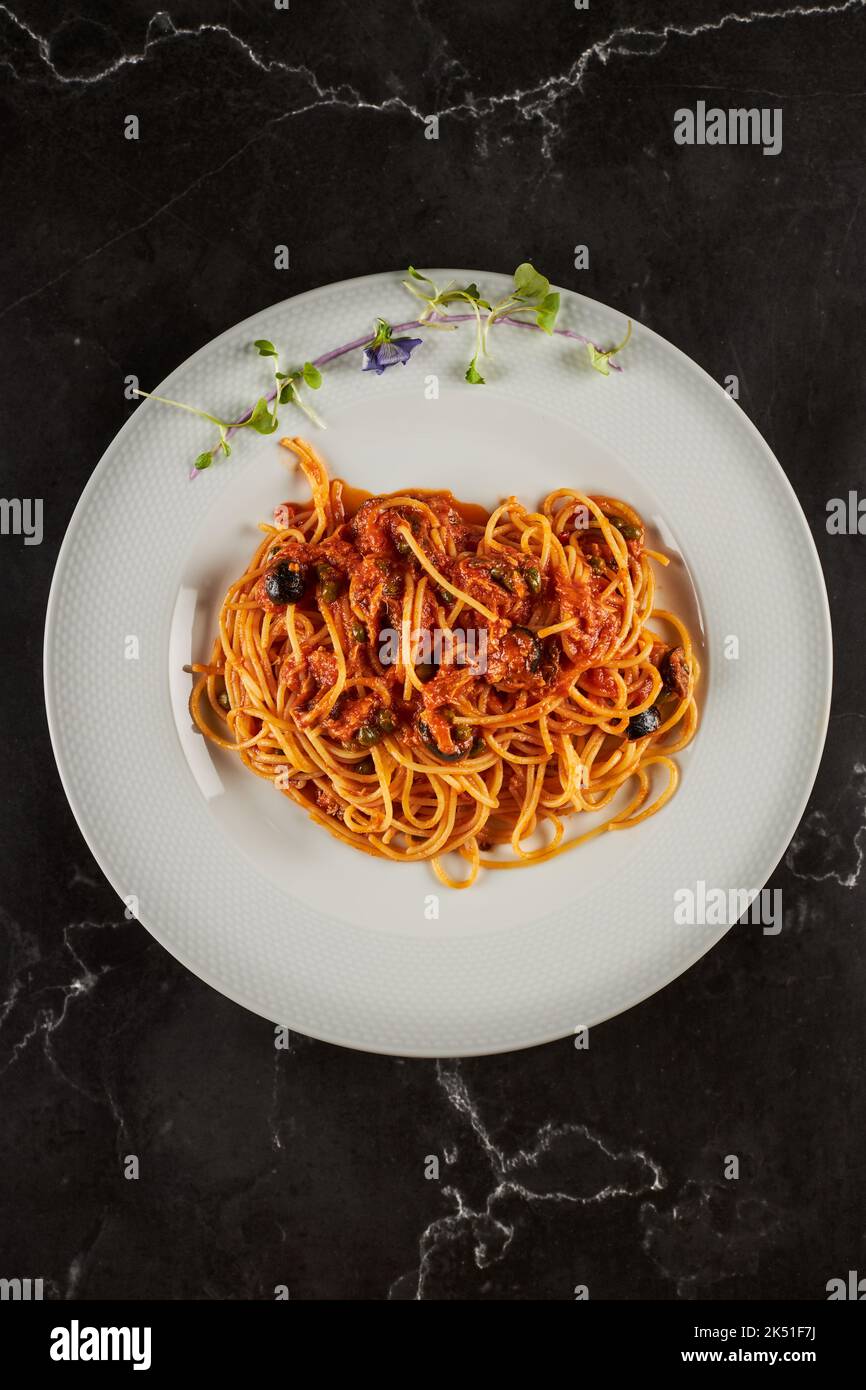 Top view of yummy spaghetti alla puttanesca dish with tomato sauce and seafood garnished with garlic and chili pepper and served on plate in Italian r Stock Photo