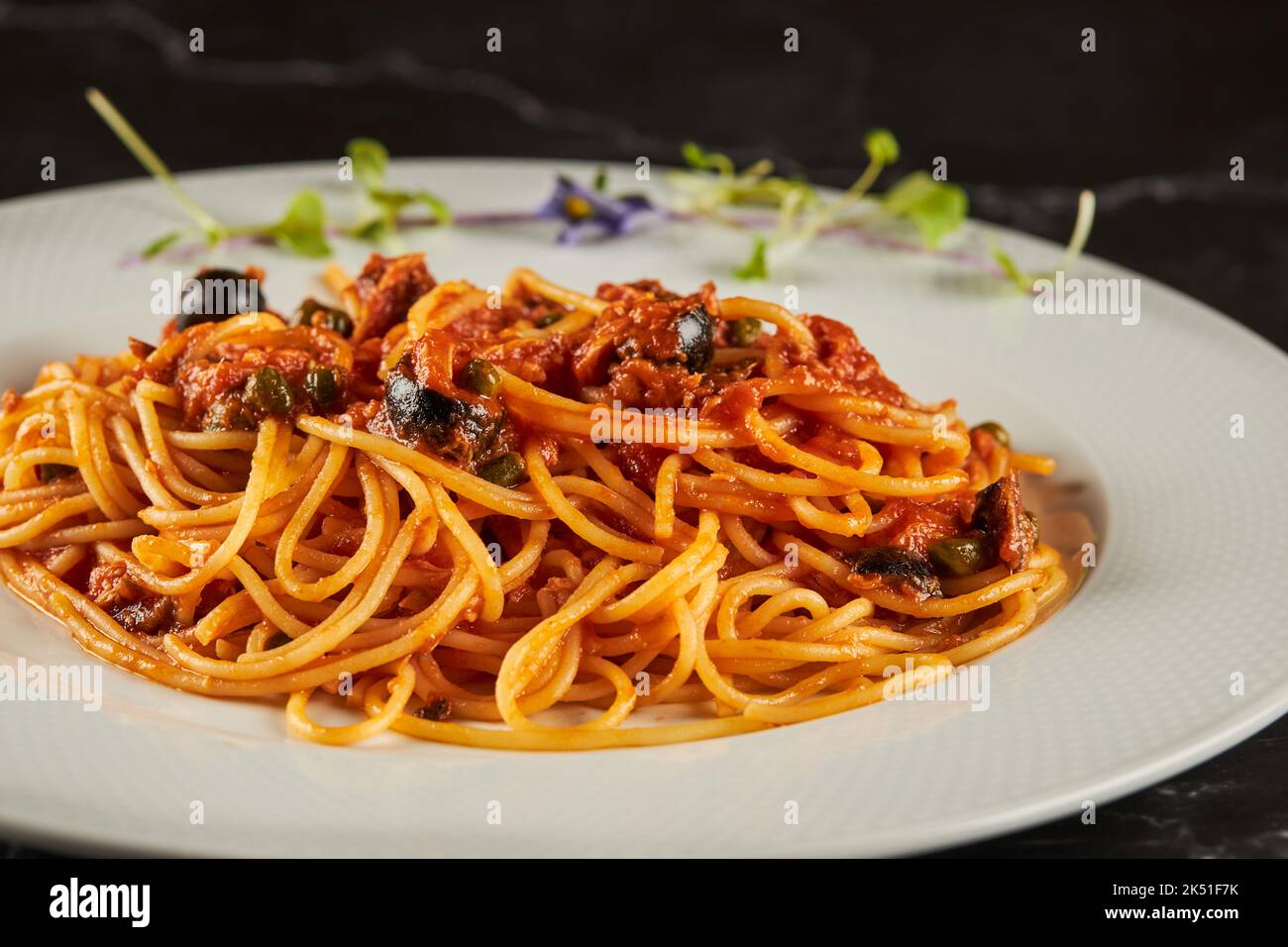 Closeup yummy spaghetti alla puttanesca dish with tomato sauce and seafood garnished with garlic and chili pepper and served on plate in Italian resta Stock Photo