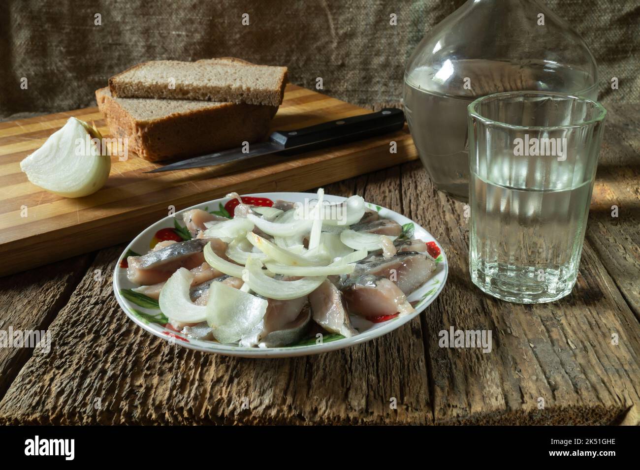 Vodka with a snack on the table. Food on a dark background. Sliced herring with onions in a plate Stock Photo