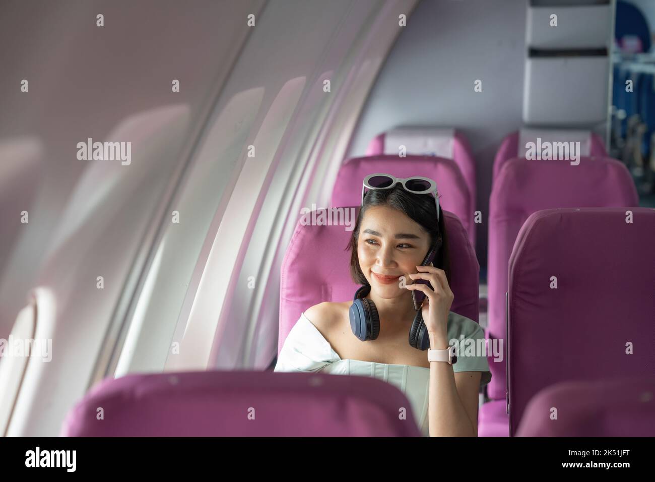 Attractive asian woman passenger of airplane calling mobile phone on board. tourism traveler concept. Stock Photo