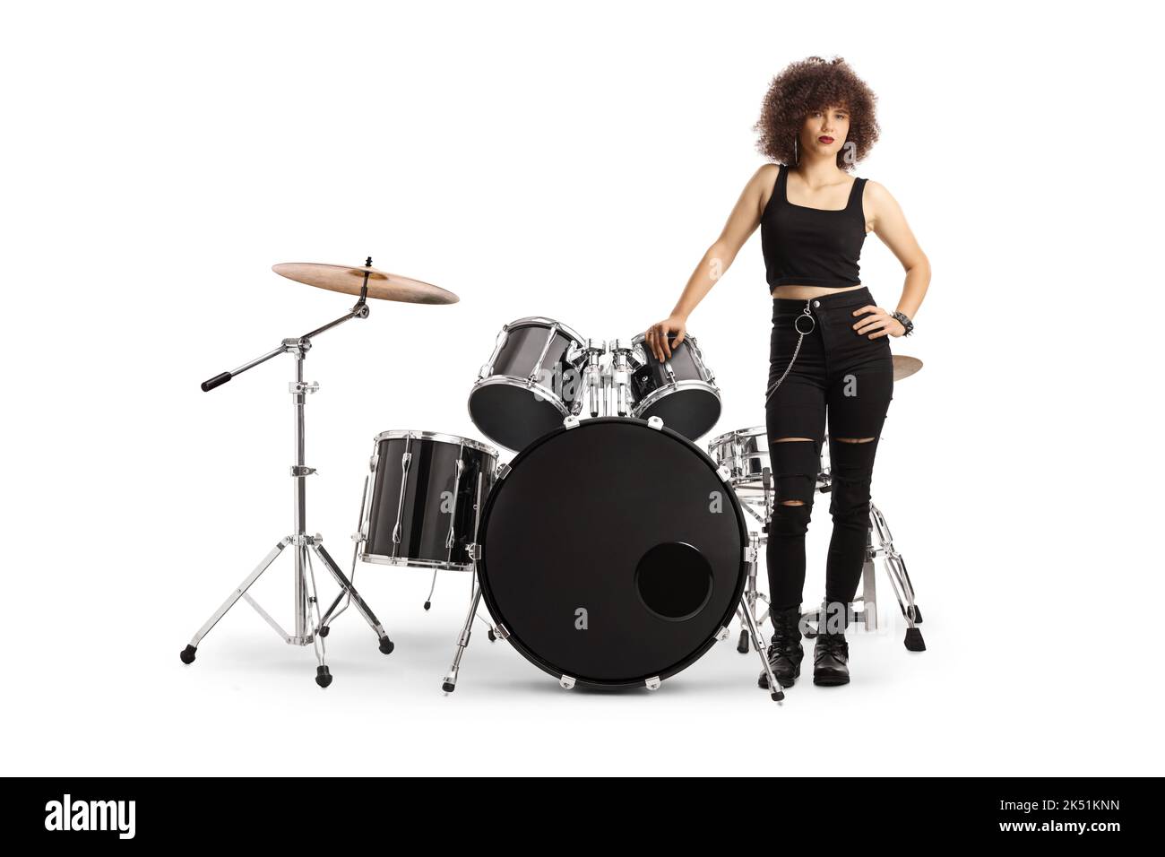 Young female drummer standing next to a drum kit isolated on white