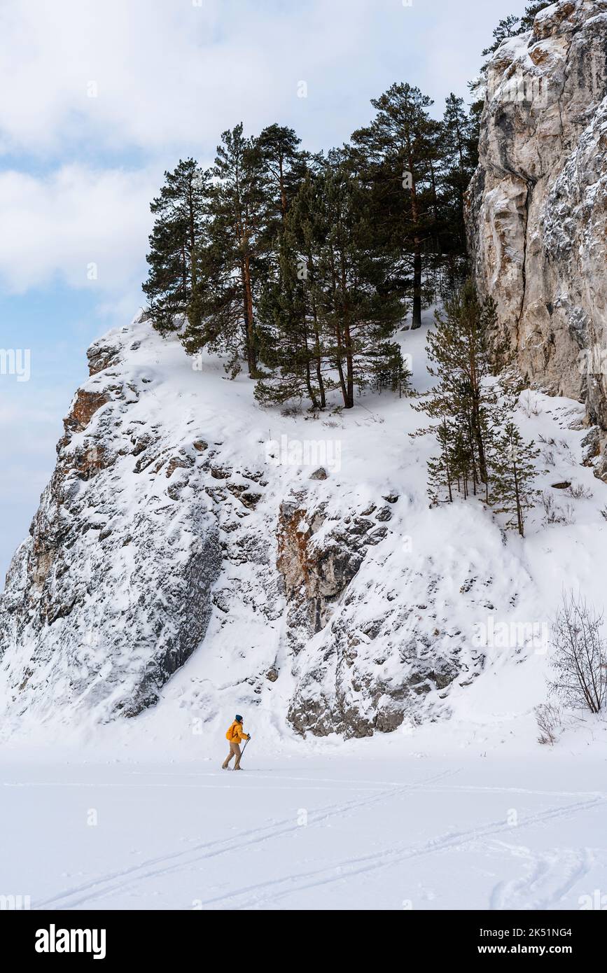 side view of young woman in yellow clothes with backpack skiing near rocks and cliffs Active healthy lifestyle Winter sports Hiking Stock Photo