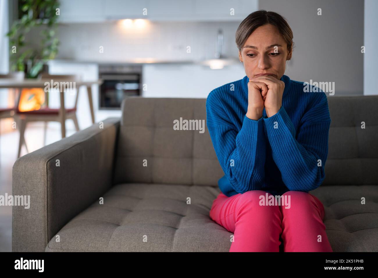 Young woman sits on sofa with depressed and tired expression after breaking up with boyfriend Stock Photo
