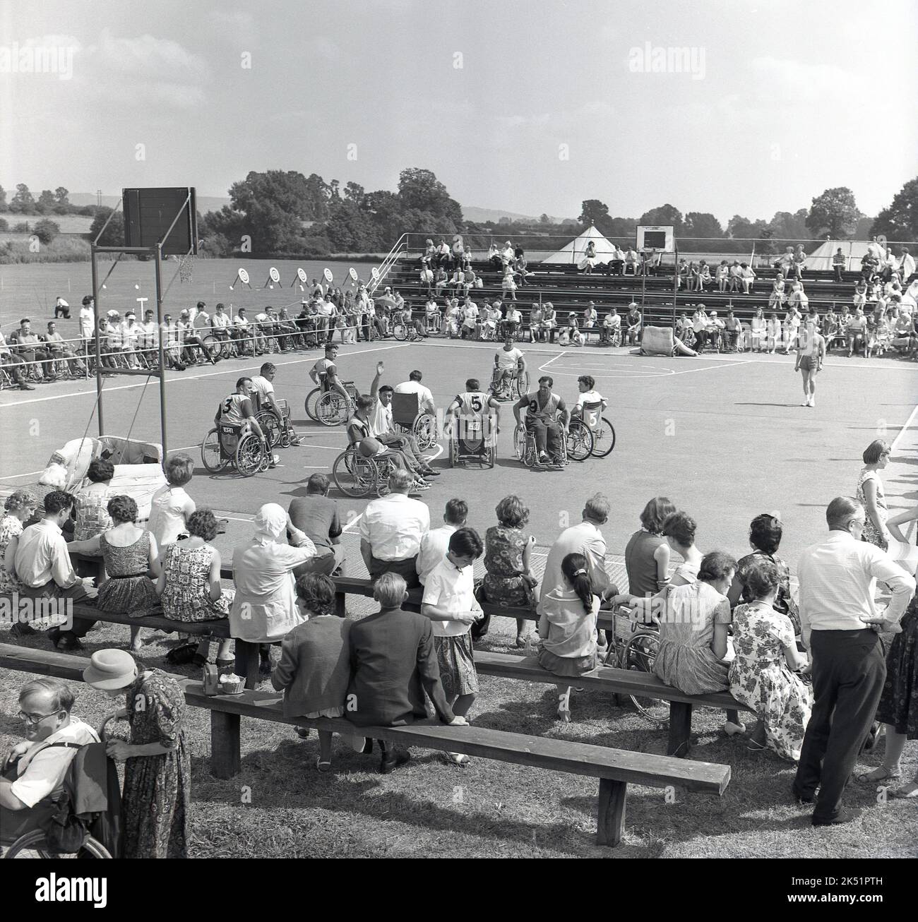 1964, historical, in the grounds of Stoke Mandeville Hospital, home of the National Spinal Injuries Centre, spectators watch wheelchair athletes compete in a basketball tournament. Stoke Mandeville in Aylesbury, Buckinghamshire, England, UK, was the birthplace of the Paralympic movement. 1948, the year of the post-war London Olympics, saw the first competition for wheelchair athletes, when 16 injured serviceman and women took part in what was known as the Stoke Mandeville Games, which later became the Paralympic Games. Stock Photo