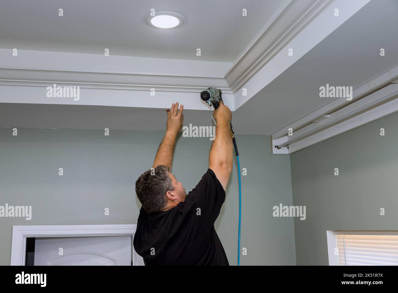 A professional carpenter nails wood crown molding between a newly
