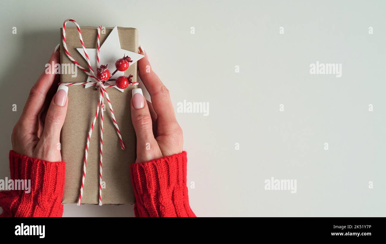 female hands red sweater hold Christmas New Year gift box on white background,top view,flat lay,copy space. Christmas holidays celebration concept,gif Stock Photo