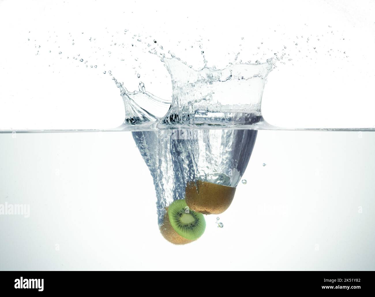 Two half kiwi splashing in water forming crown splash. On white background. Stock Photo